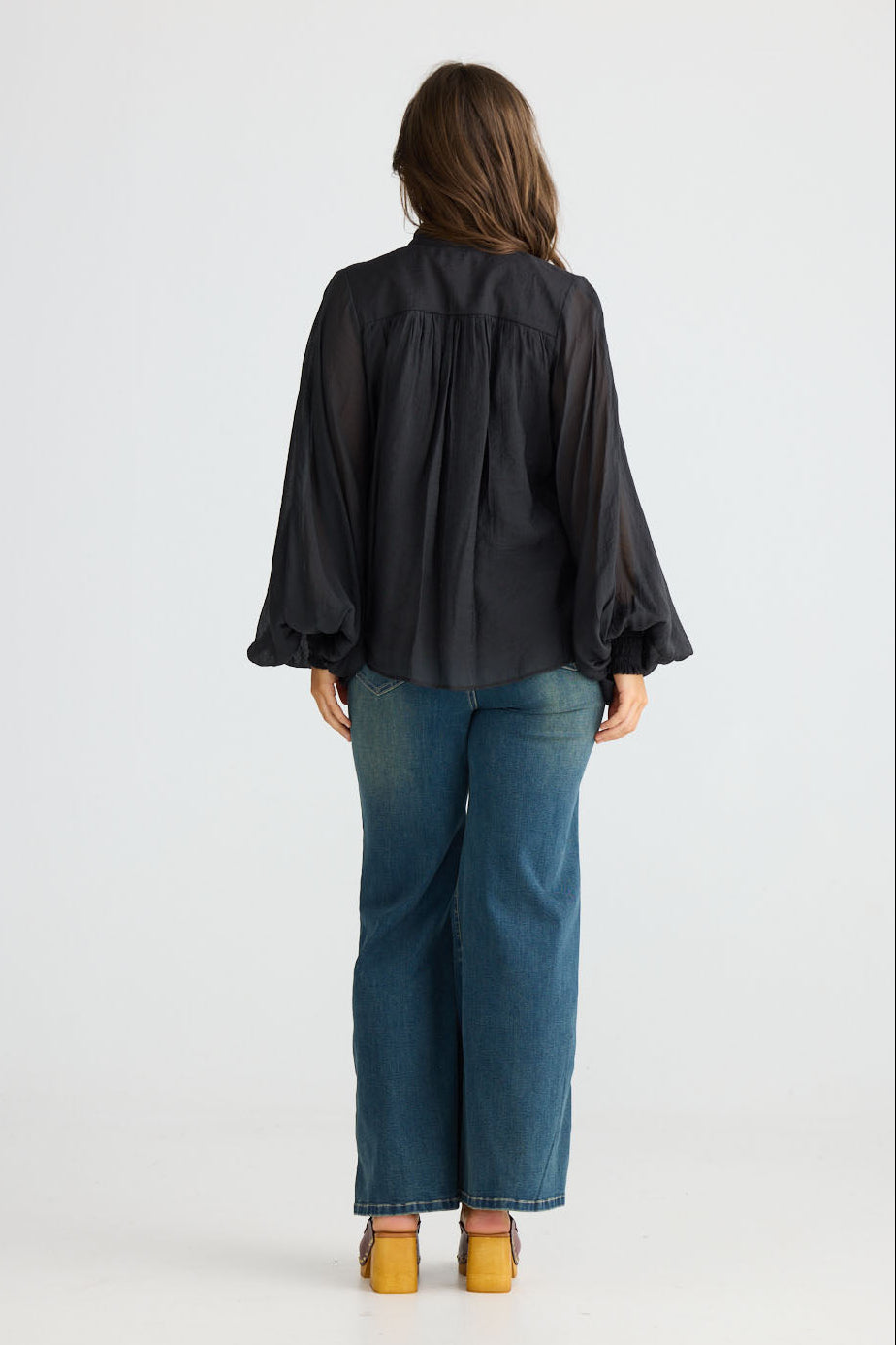 Model wearing Sylva Blouse in black with high collar with ruched details, side view on white background
