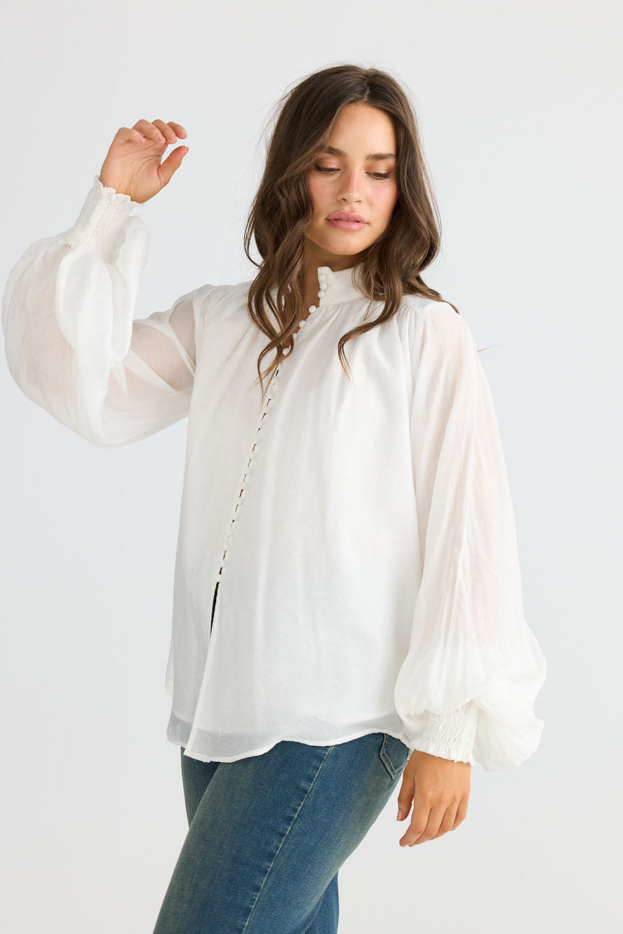 Model wearing Sylva Blouse in off white with high collar with ruched details, front view on white background