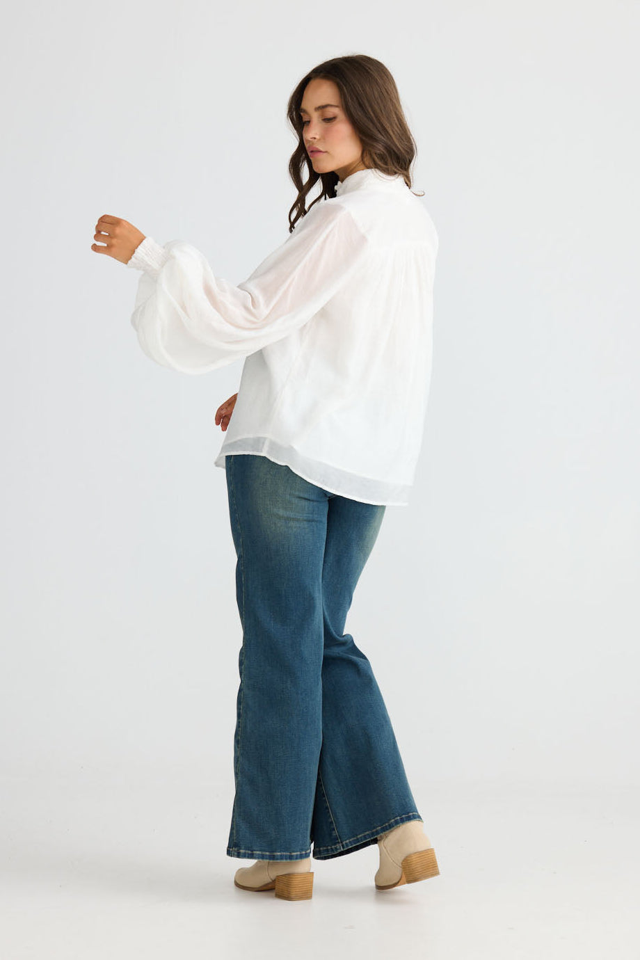 Model wearing Sylva Blouse in off white with high collar with ruched details, back view on white background