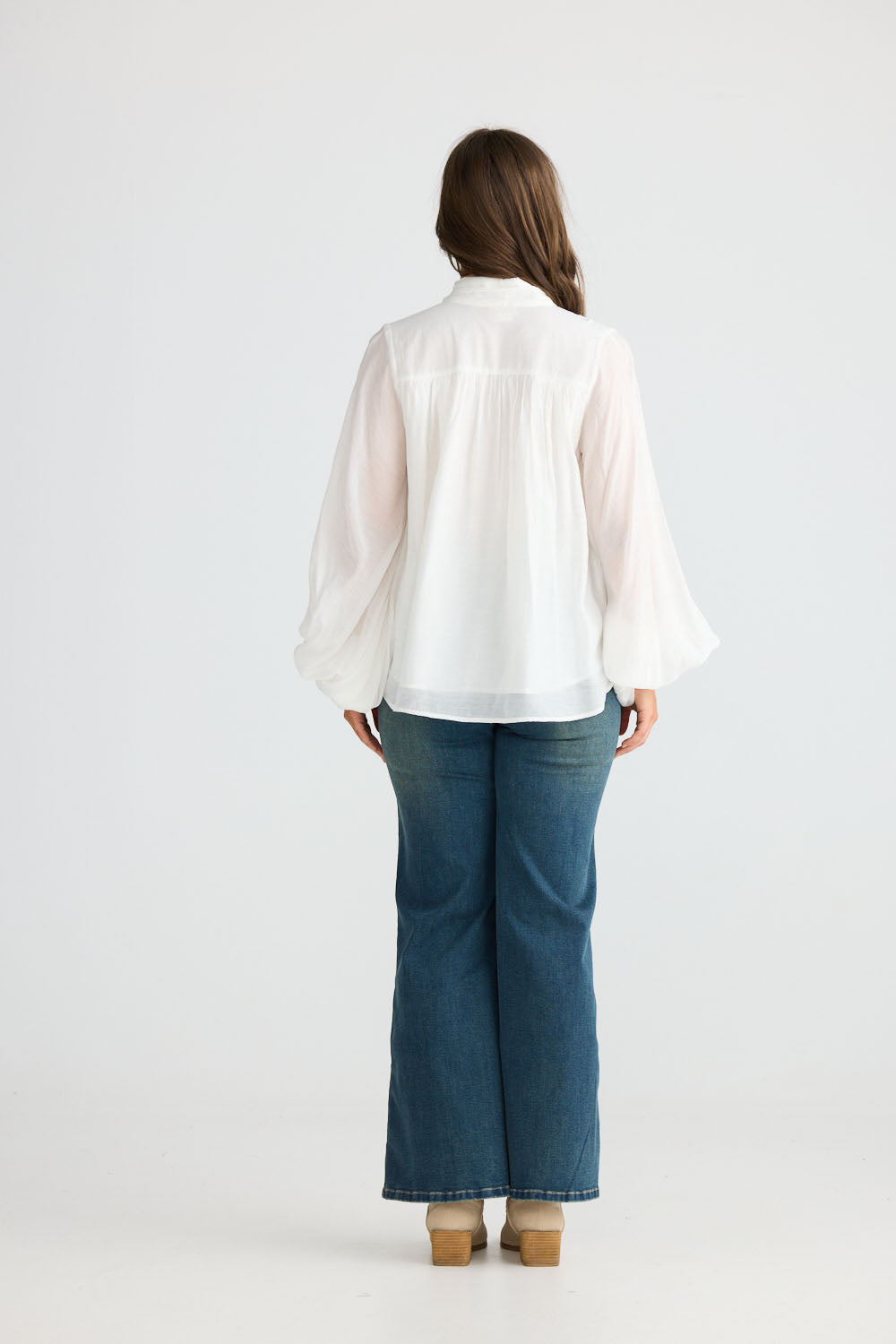 Model wearing Sylva Blouse in off white with high collar with ruched details, side view on white background