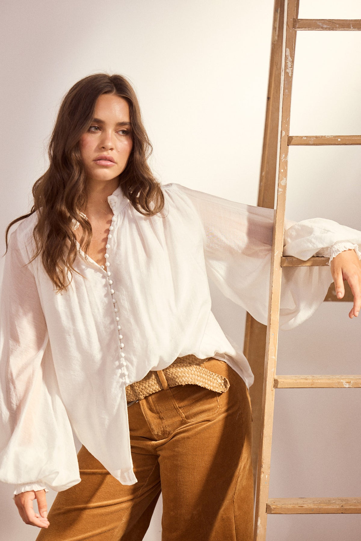 Model wearing Sylva Blouse in off white with high collar with ruched details, back view on white background