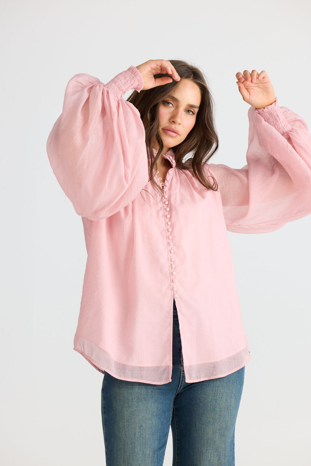 Model wearing Sylva Blouse in pink with high collar with ruched details, side view on white background