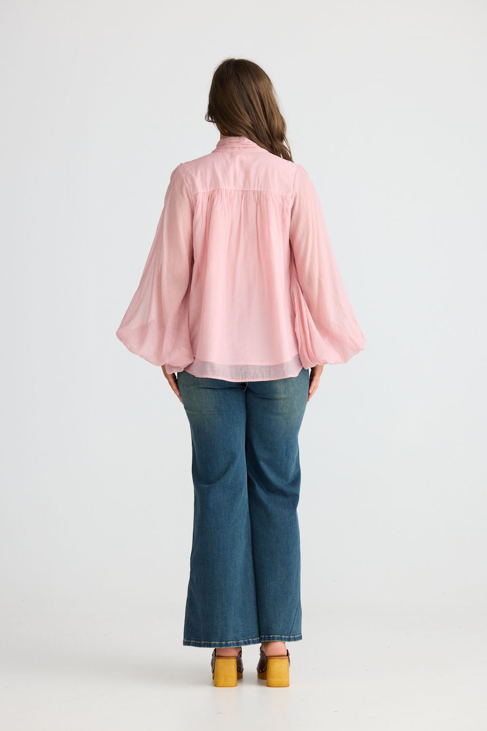 Model wearing Sylva Blouse in pink with high collar with ruched details, side view on white background