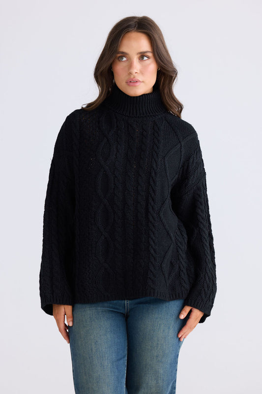 Model wearing Dixie Knit in black with roll-neck collar and cable knit design, back view on white background
