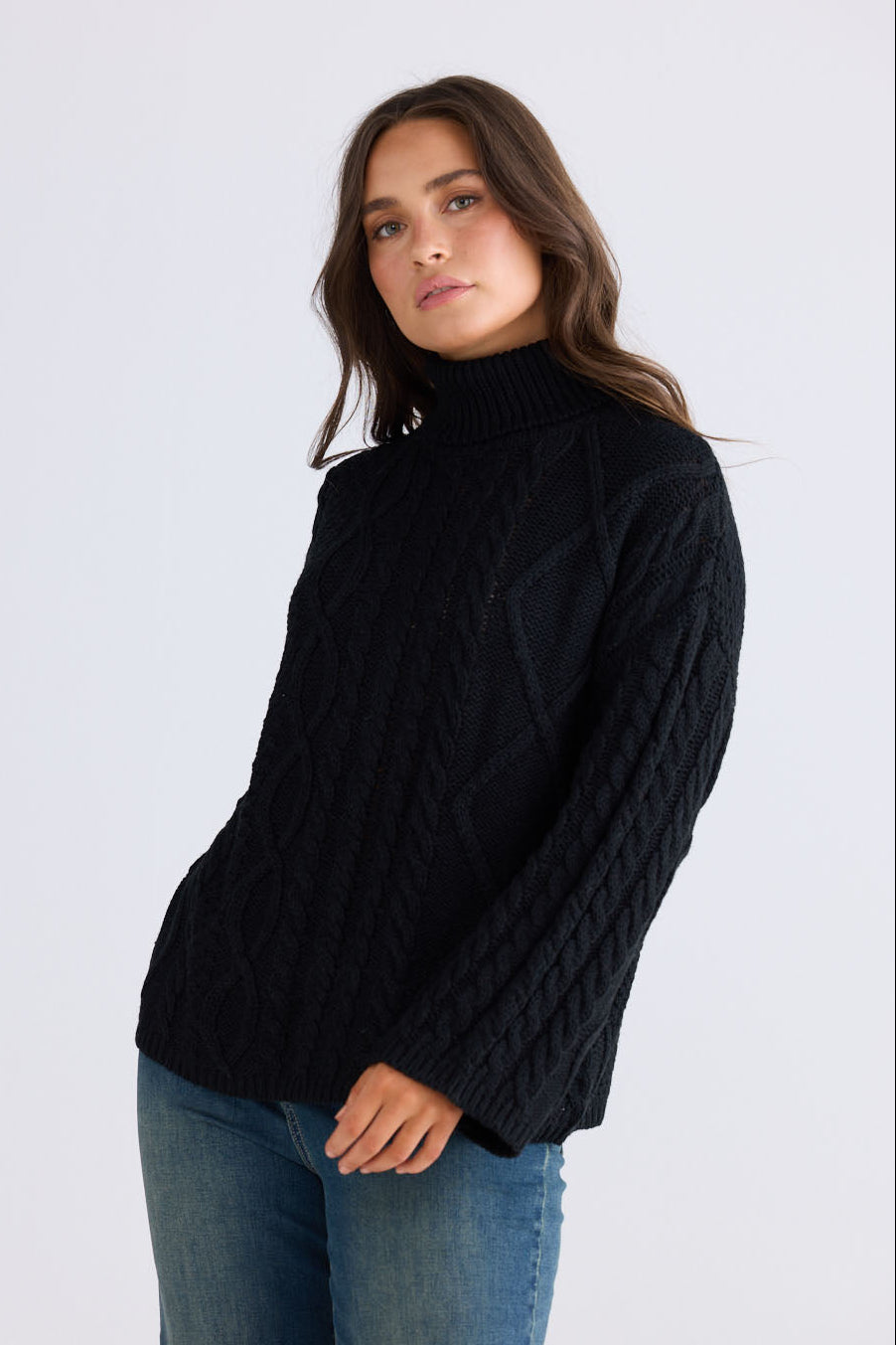 Model wearing Dixie Knit in black with roll-neck collar and cable knit design, side view on white background