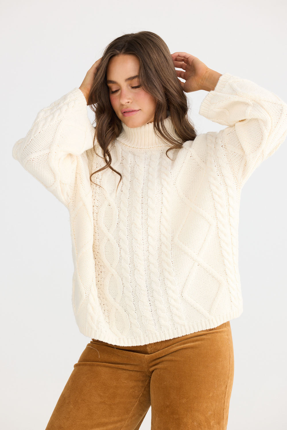 Model wearing Dixie Knit in cream with roll-neck collar and cable knit design, front view on white background