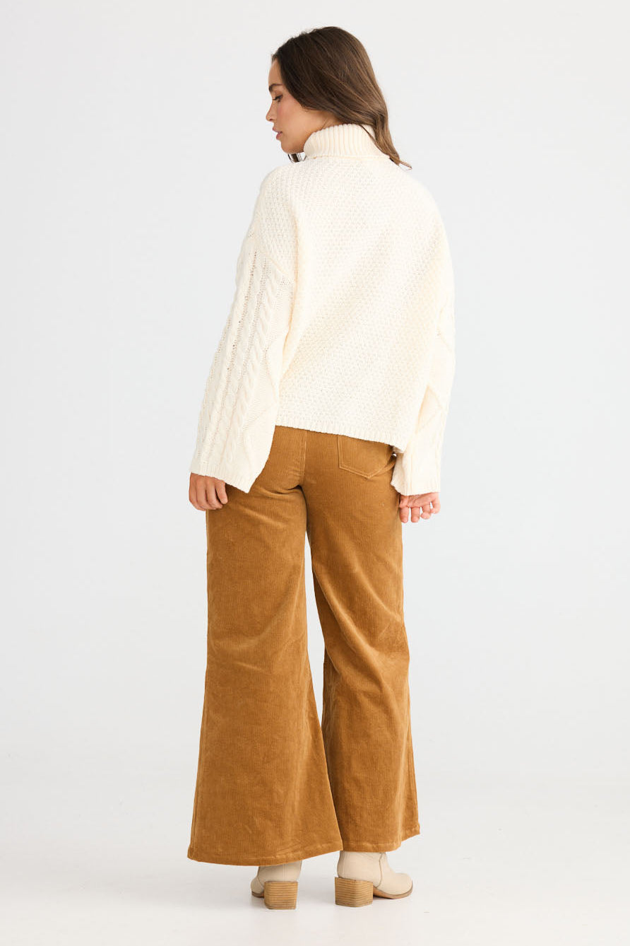 Model wearing Dixie Knit in cream with roll-neck collar and cable knit design, front view on white background