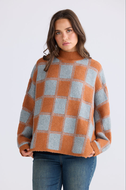 Model wearing Nyx Knit in teal and ochre with mock neck and dolman sleeve, back view on white background