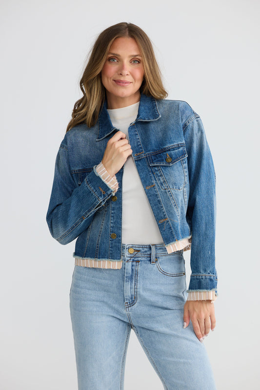 Model wearing Riverstone Jacket in mid blue wash with classic denim silhouette, front view on white background