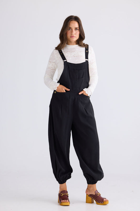 Model wearing Genie Overalls in black, front view on white background