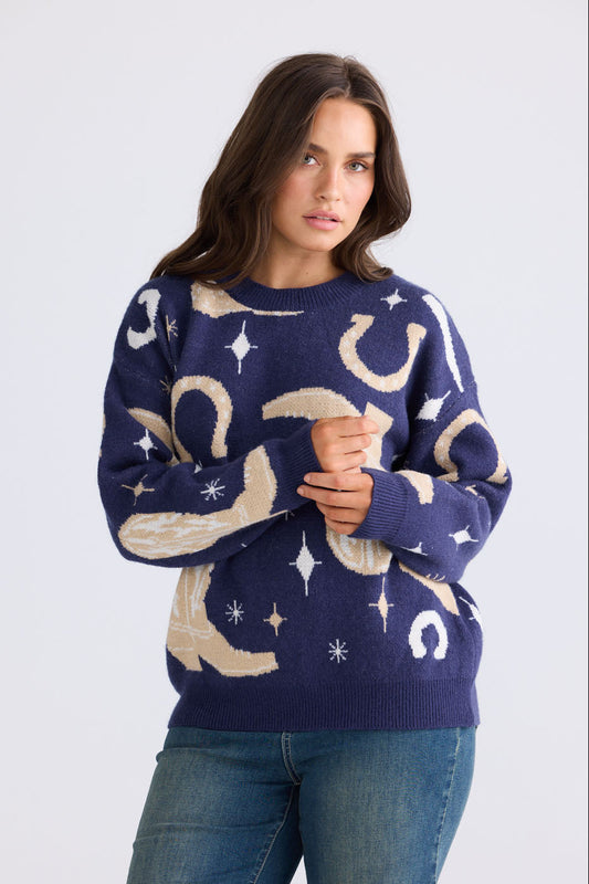 Model wearing Lucky Boots Knit in navy with ribbed neckline and cowboy-themed print, side view on white background