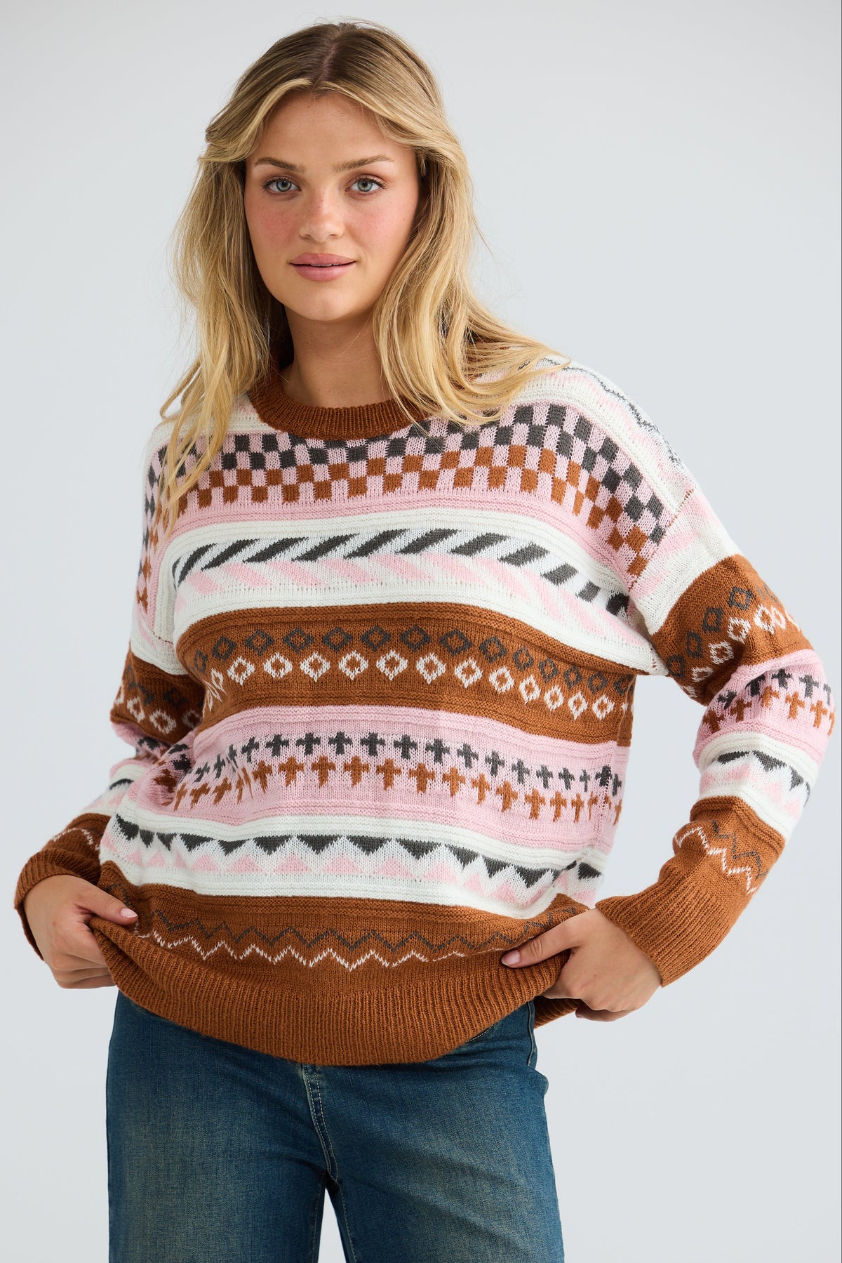 Woman wearing a patterned sweater and jeans on a plain background