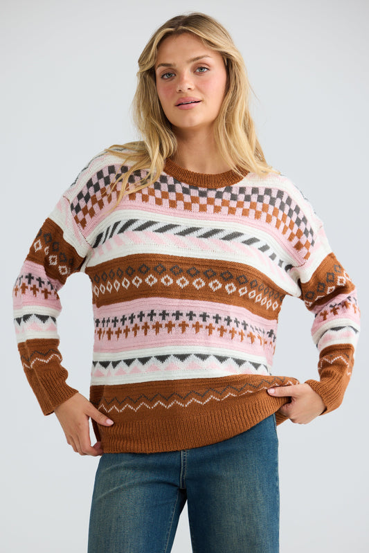 Woman wearing a patterned sweater and jeans on a plain background