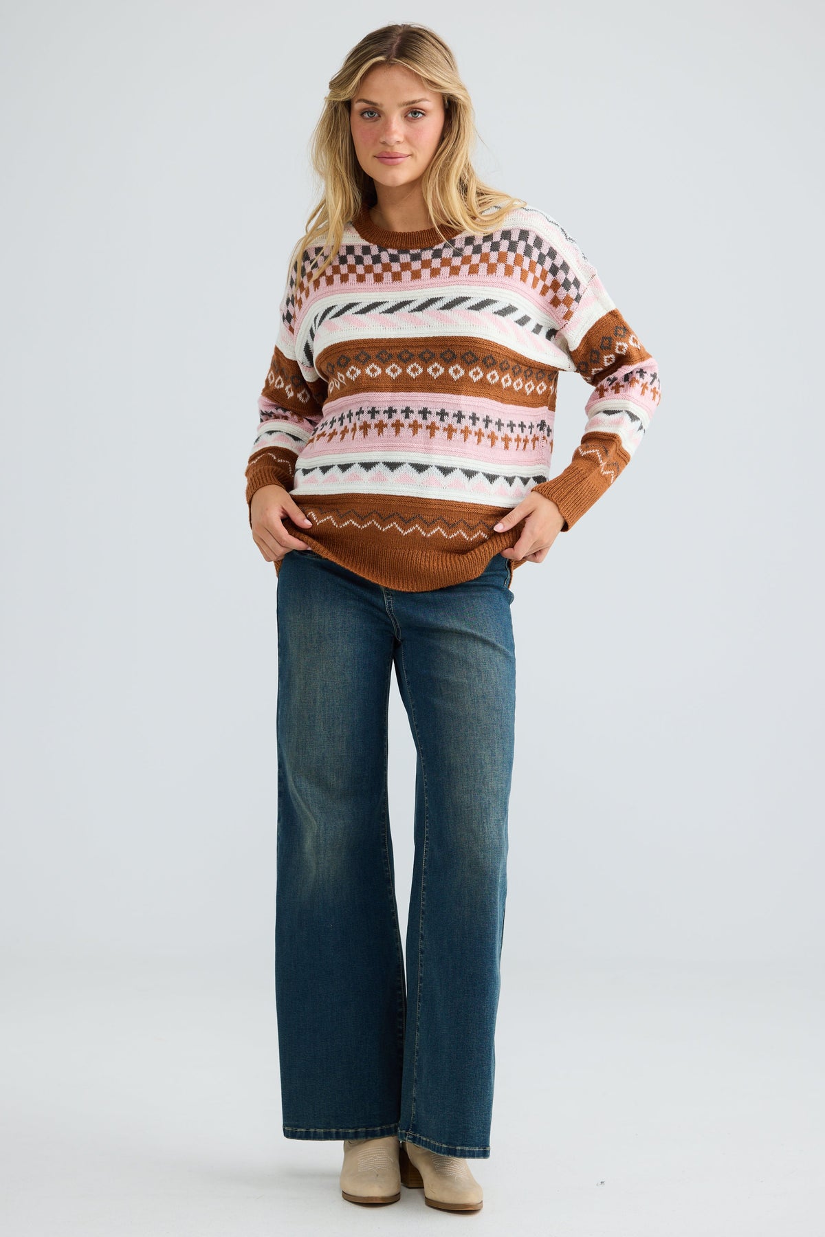 Woman wearing a patterned sweater and blue jeans on a white background