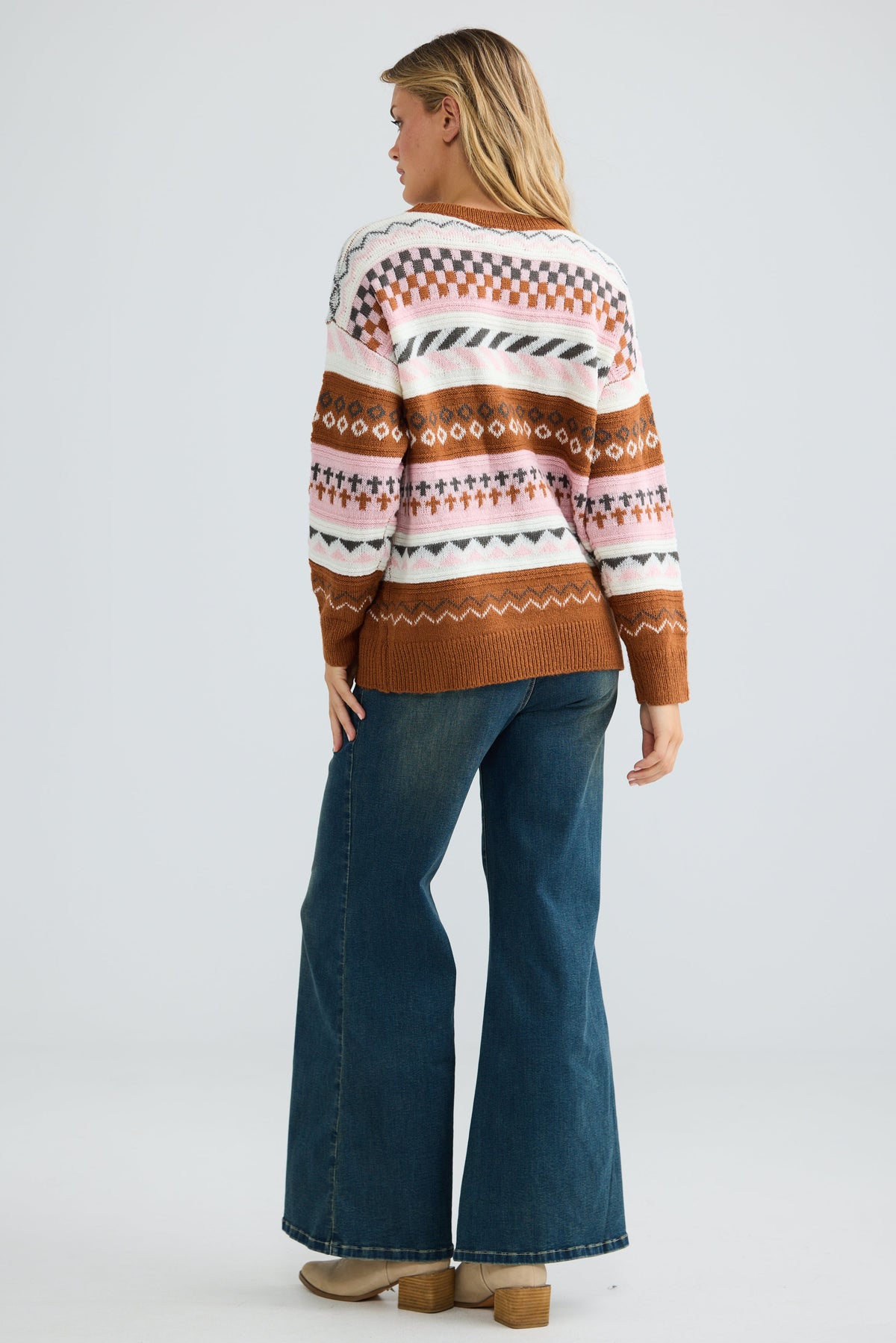 Person wearing a patterned sweater and blue jeans on a white background