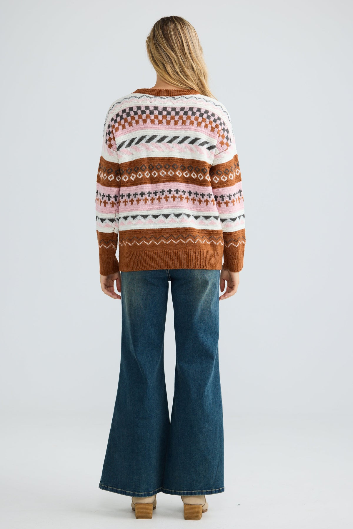 Person wearing a patterned sweater and blue jeans on a white background