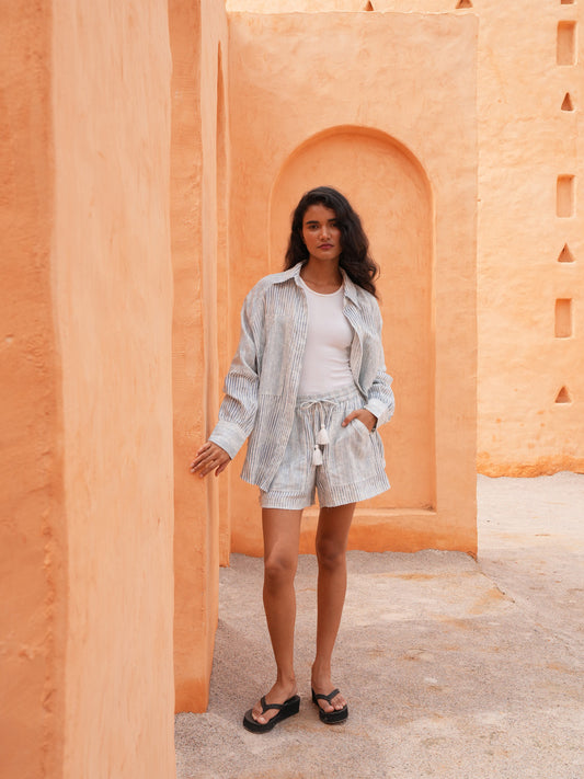 Bodhi Shirt in blue stripe worn open over a white tank with the matching Bodhi Short, full length in a terracotta archway.