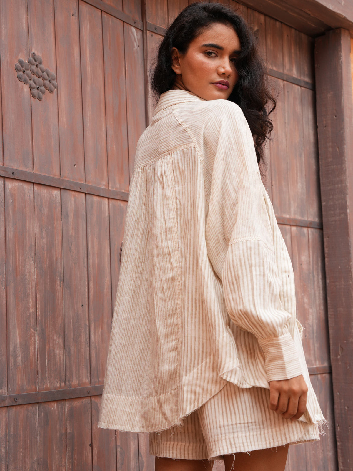 Bodhi Shirt in natural stripe, back view against a weathered timber door.