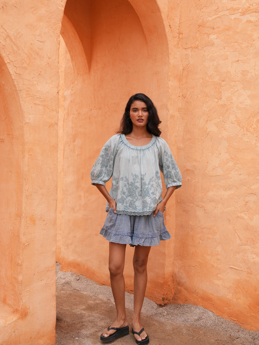 Ithika Short in steel blue with the Thistle Top in powder blue, against a terracotta wall.