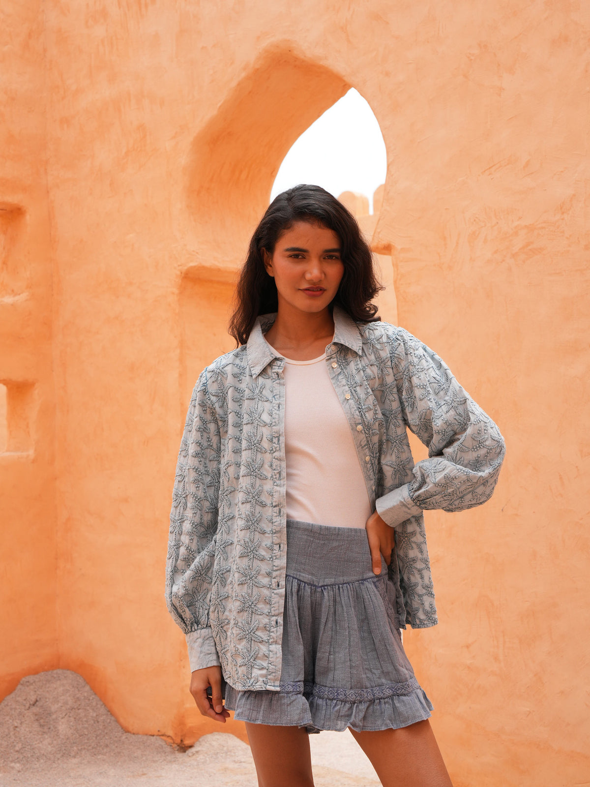 Flower Child Shirt in powder blue worn open with the Ithika Short, front view against a terracotta wall.