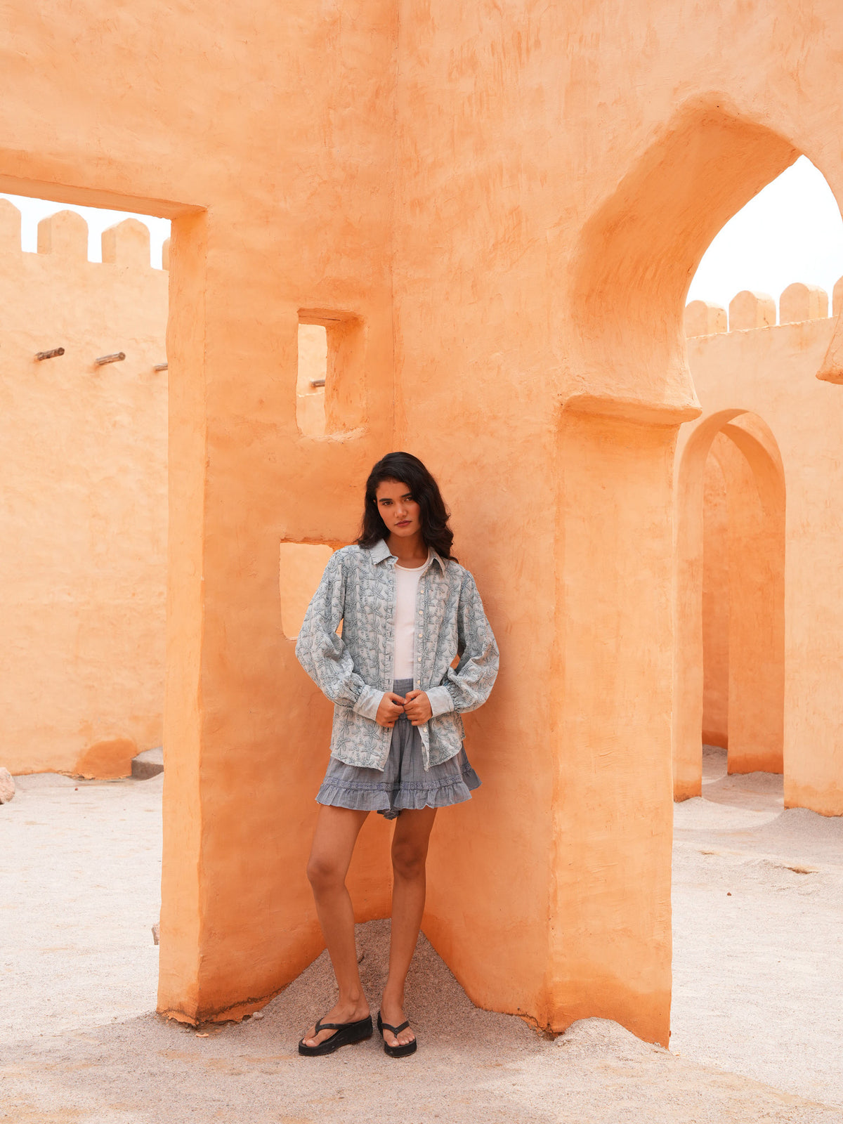 Flower Child Shirt in powder blue worn open over a white tank with the Ithika Short, full length in a terracotta archway.