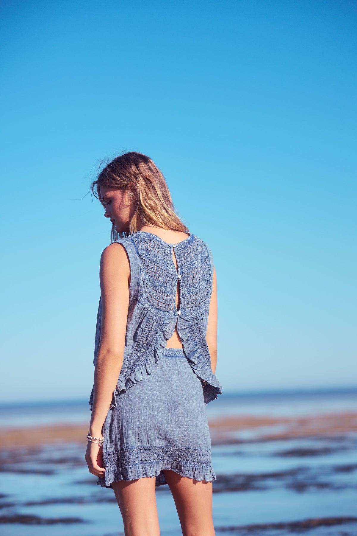 Freesia Mini Wrap Skirt and Freesia Top in steel blue, back view on the shore.
