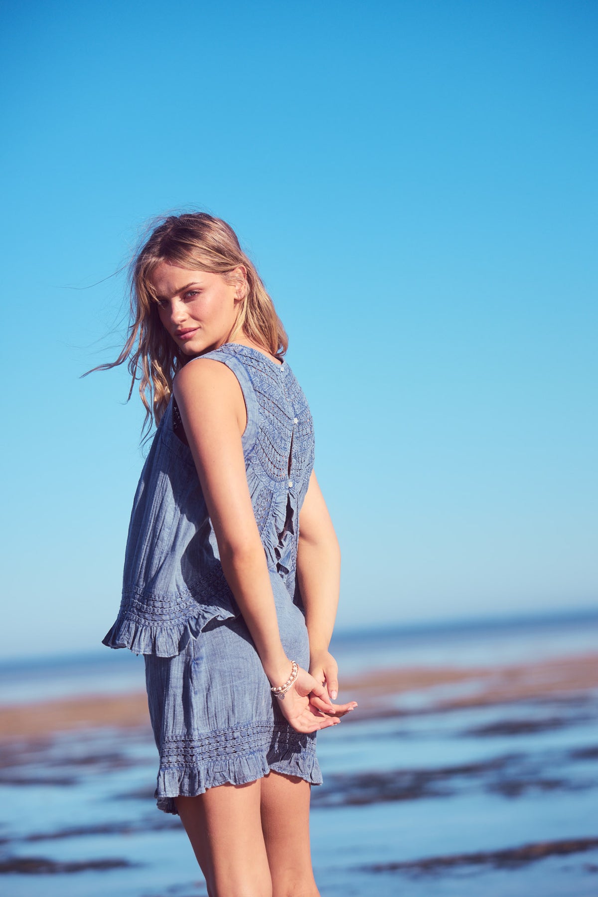 Freesia Top in steel blue, side back view on the shore.