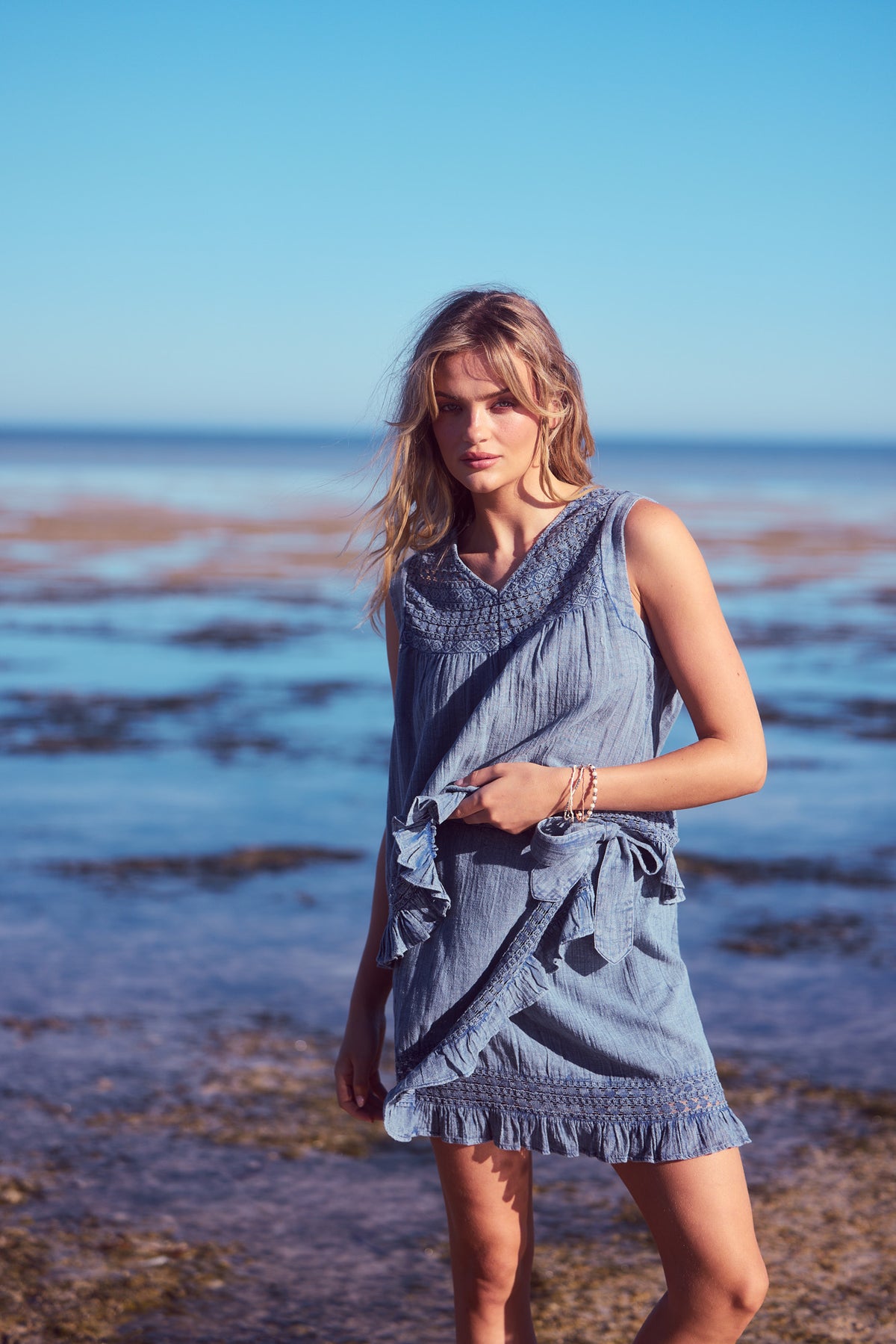 Freesia Mini Wrap Skirt and Freesia Top in steel blue, on the shore under a blue sky.