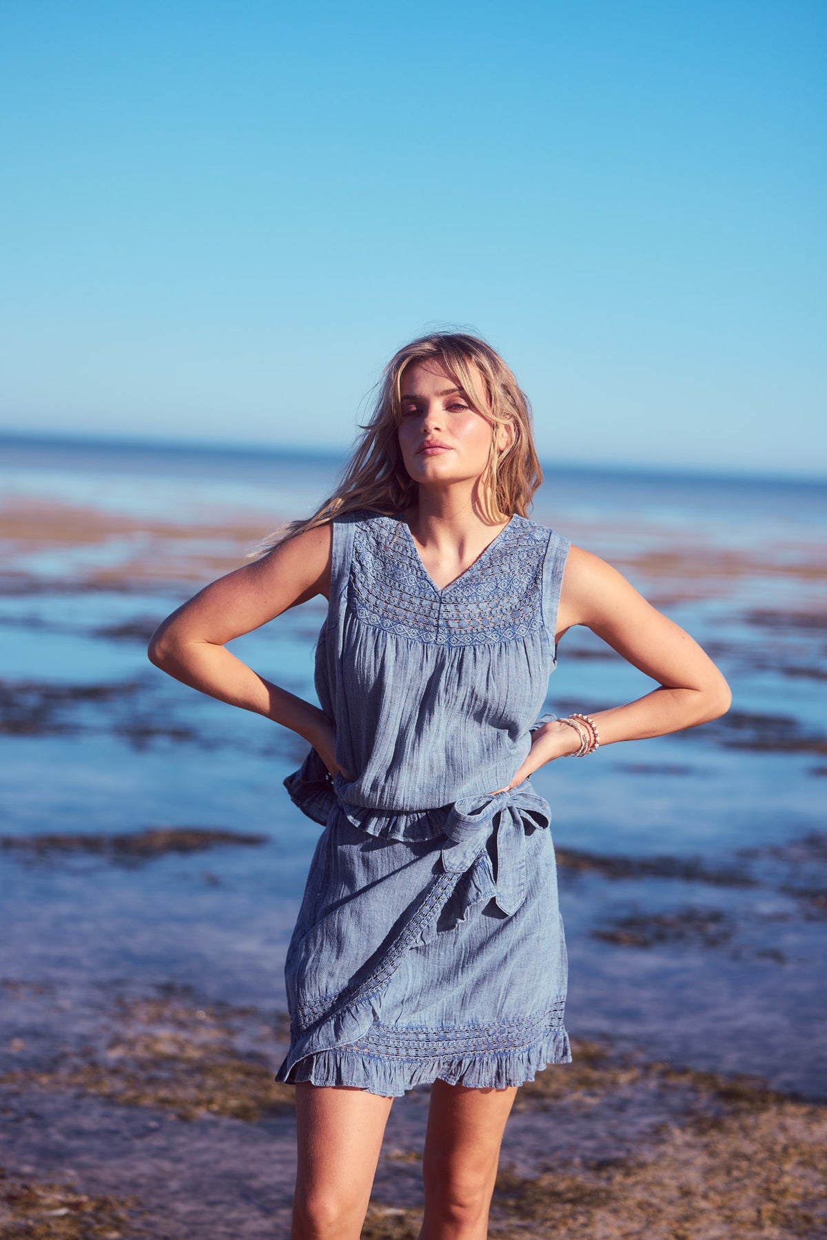 Freesia Top and skirt set in steel blue, hands on hips by the sea.