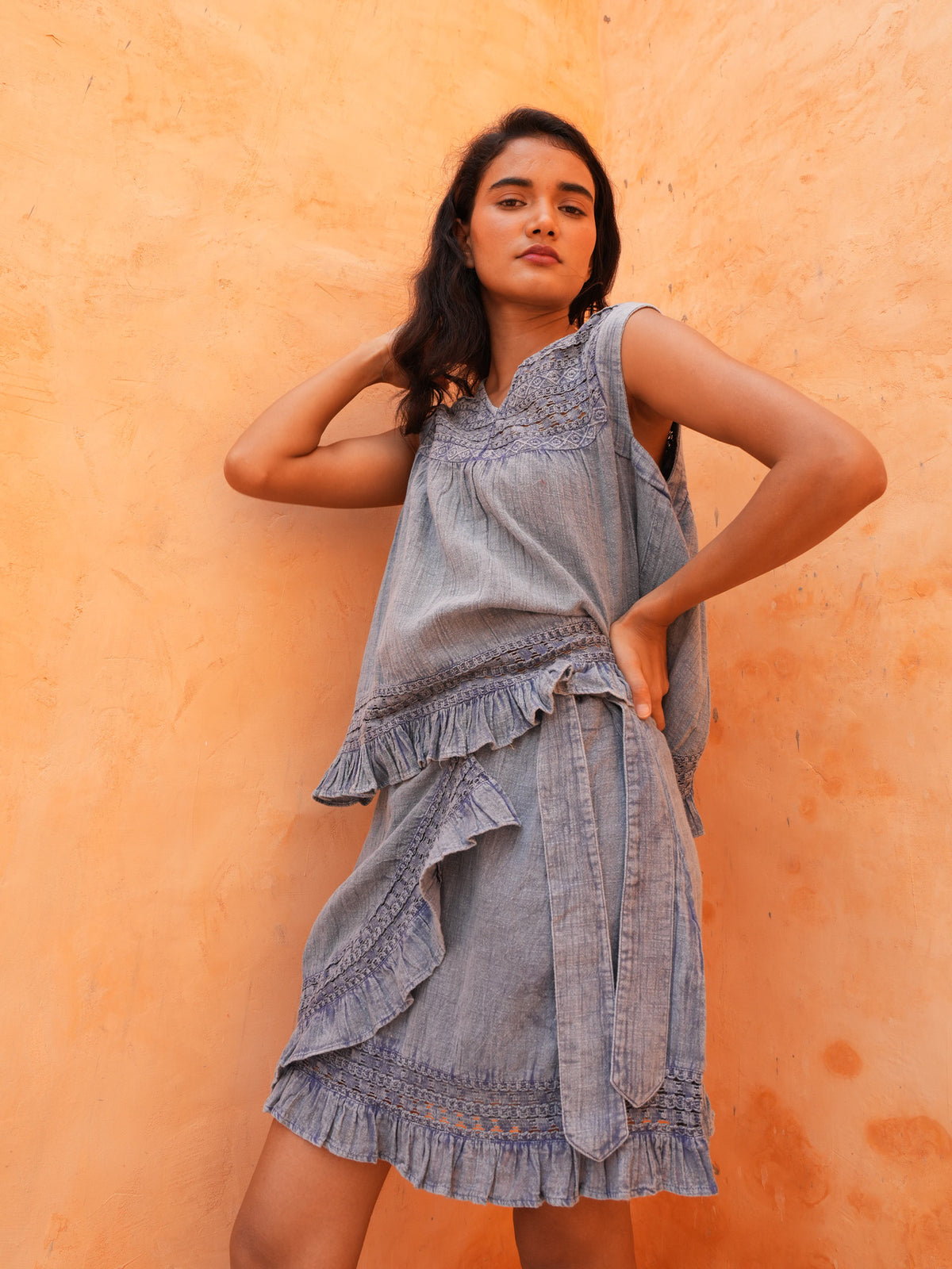 Freesia Mini Wrap Skirt in steel blue worn with the matching Freesia Top, against a terracotta wall.
