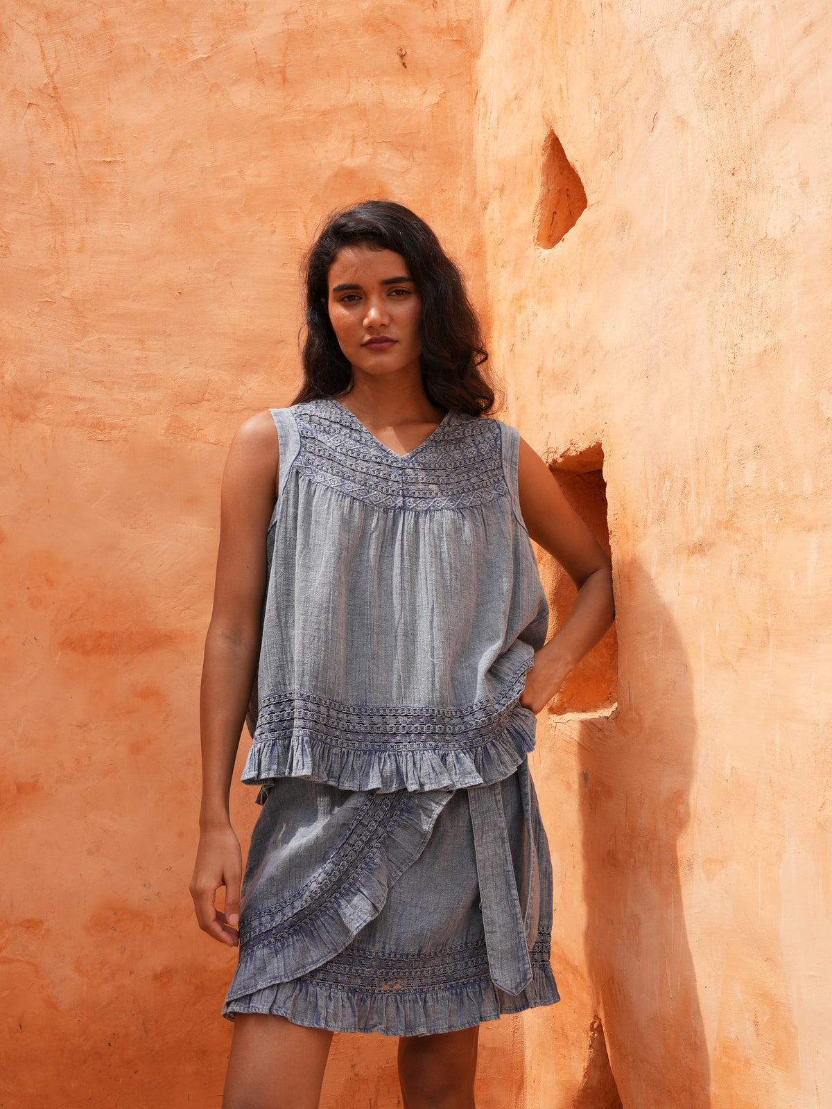 Freesia Top in steel blue with matching steel blue bottoms, front view against a terracotta wall.