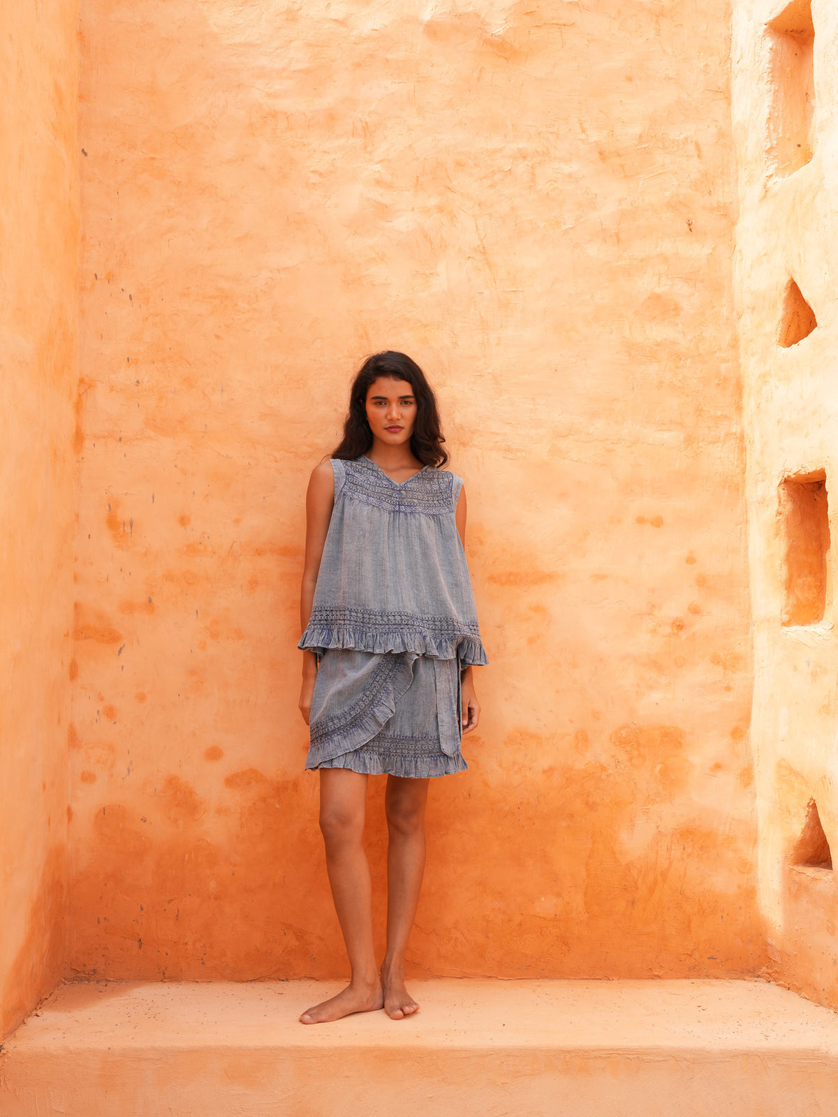Freesia Mini Wrap Skirt and Freesia Top in steel blue, full length in a terracotta courtyard.