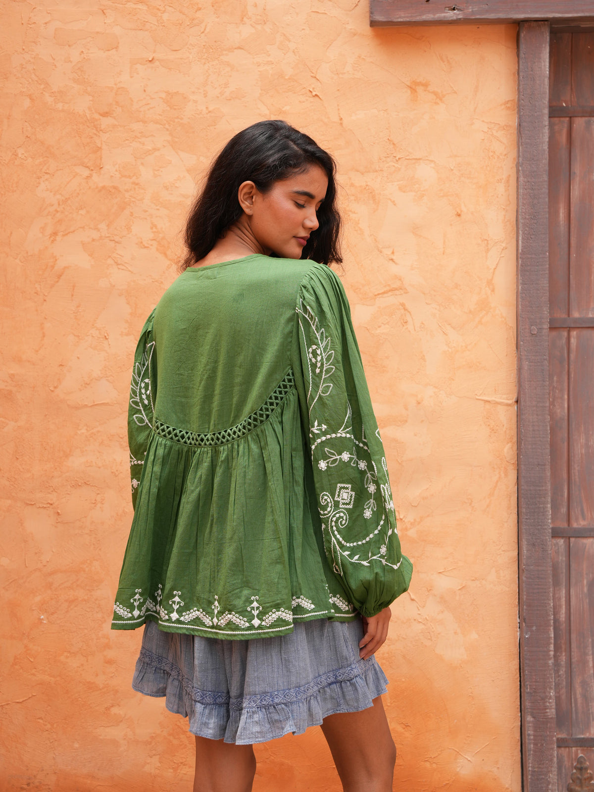 Sapphire Top in olive, three-quarter back view against a terracotta wall.