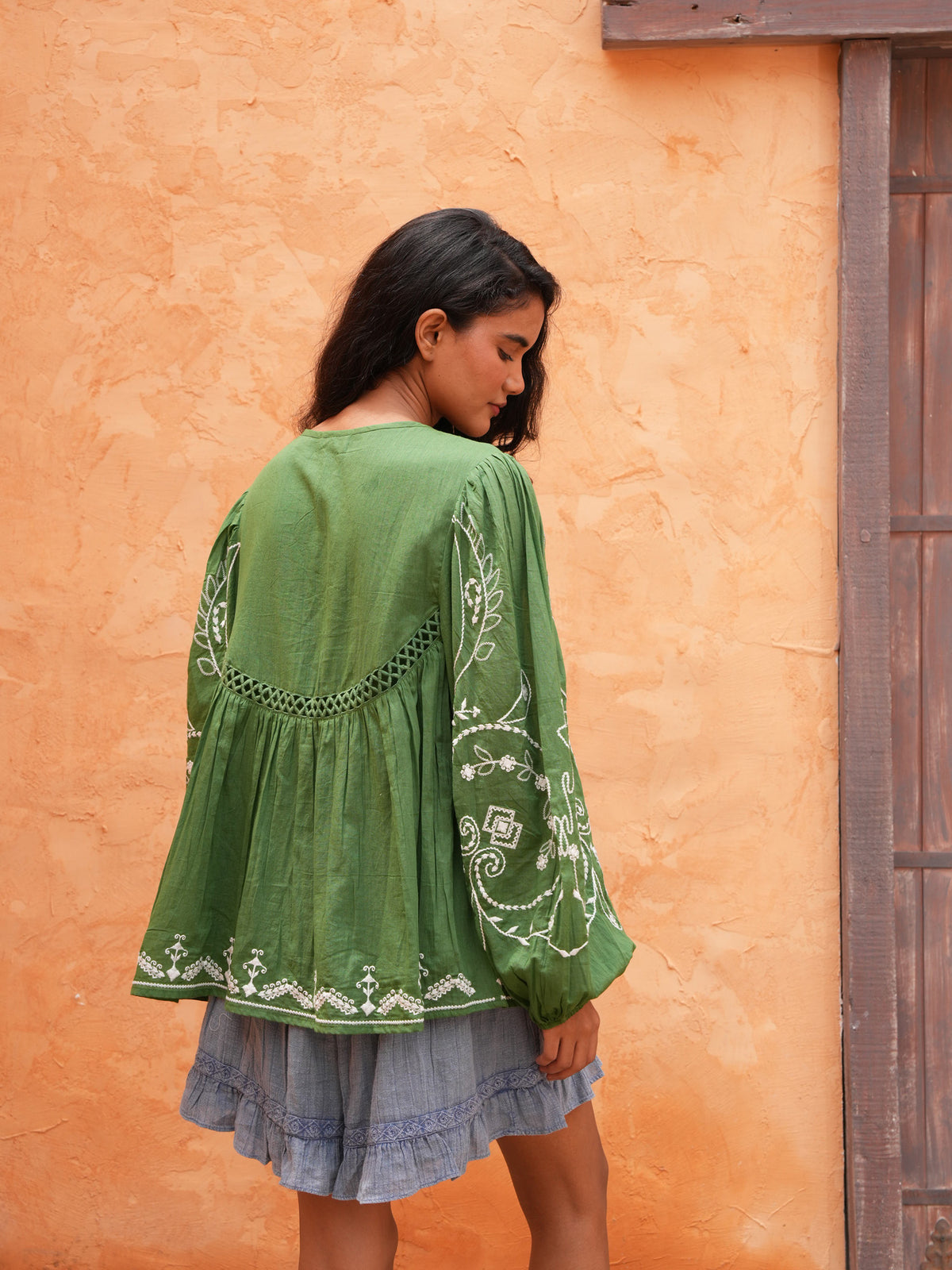Ithika Short in steel blue with the Sapphire Top, back view against a terracotta wall.