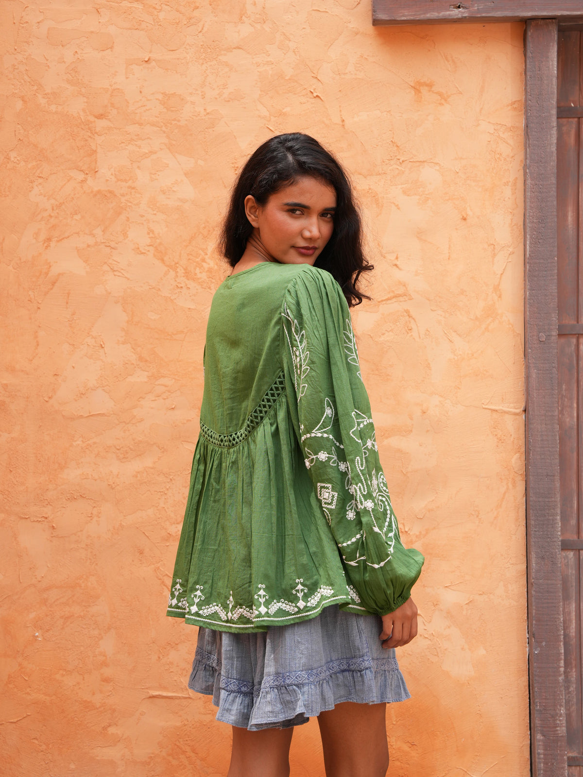Sapphire Top in olive, back view against a terracotta wall.