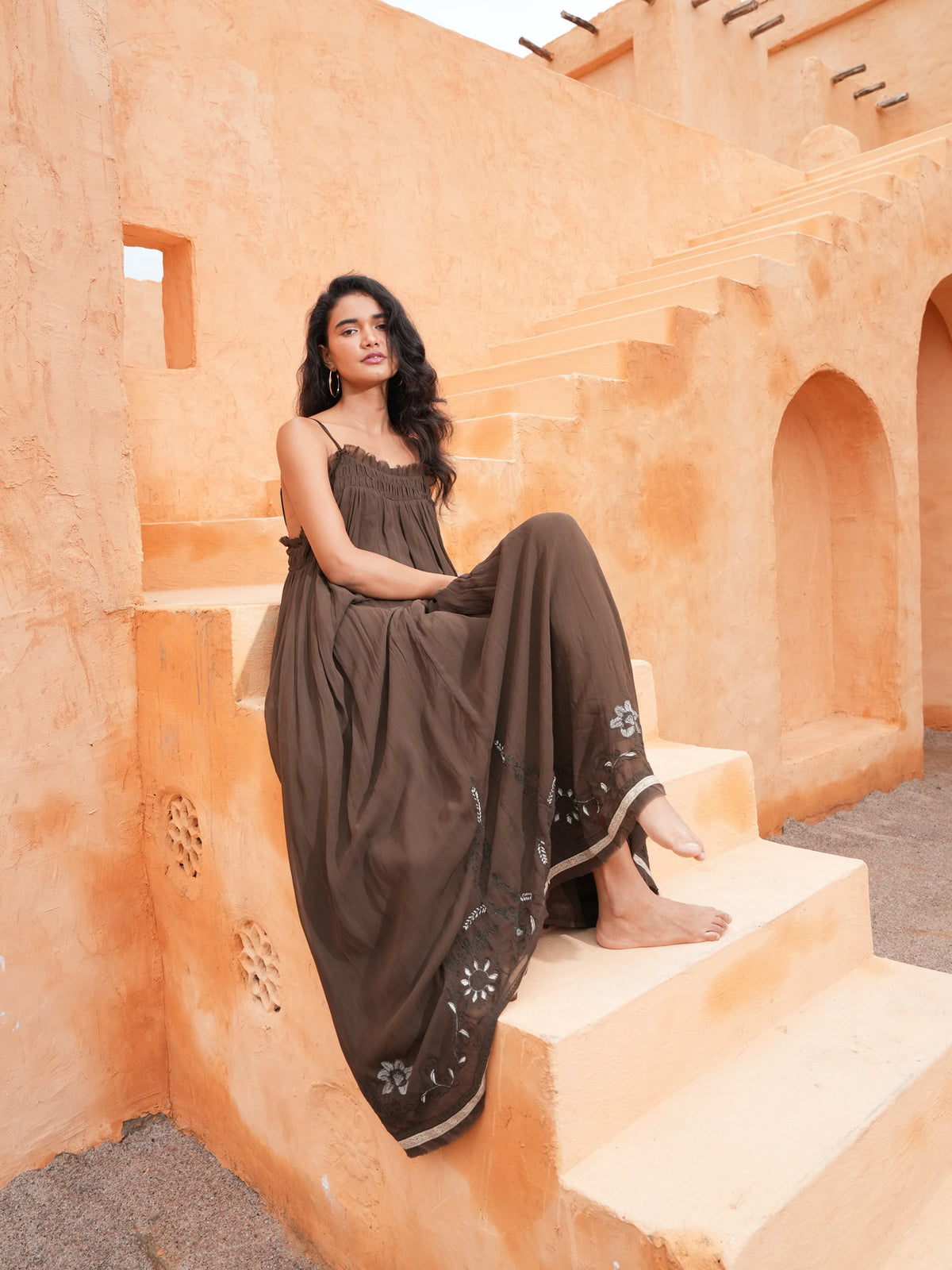 Ambrosia Maxi Dress in cocoa, seated on terracotta steps.