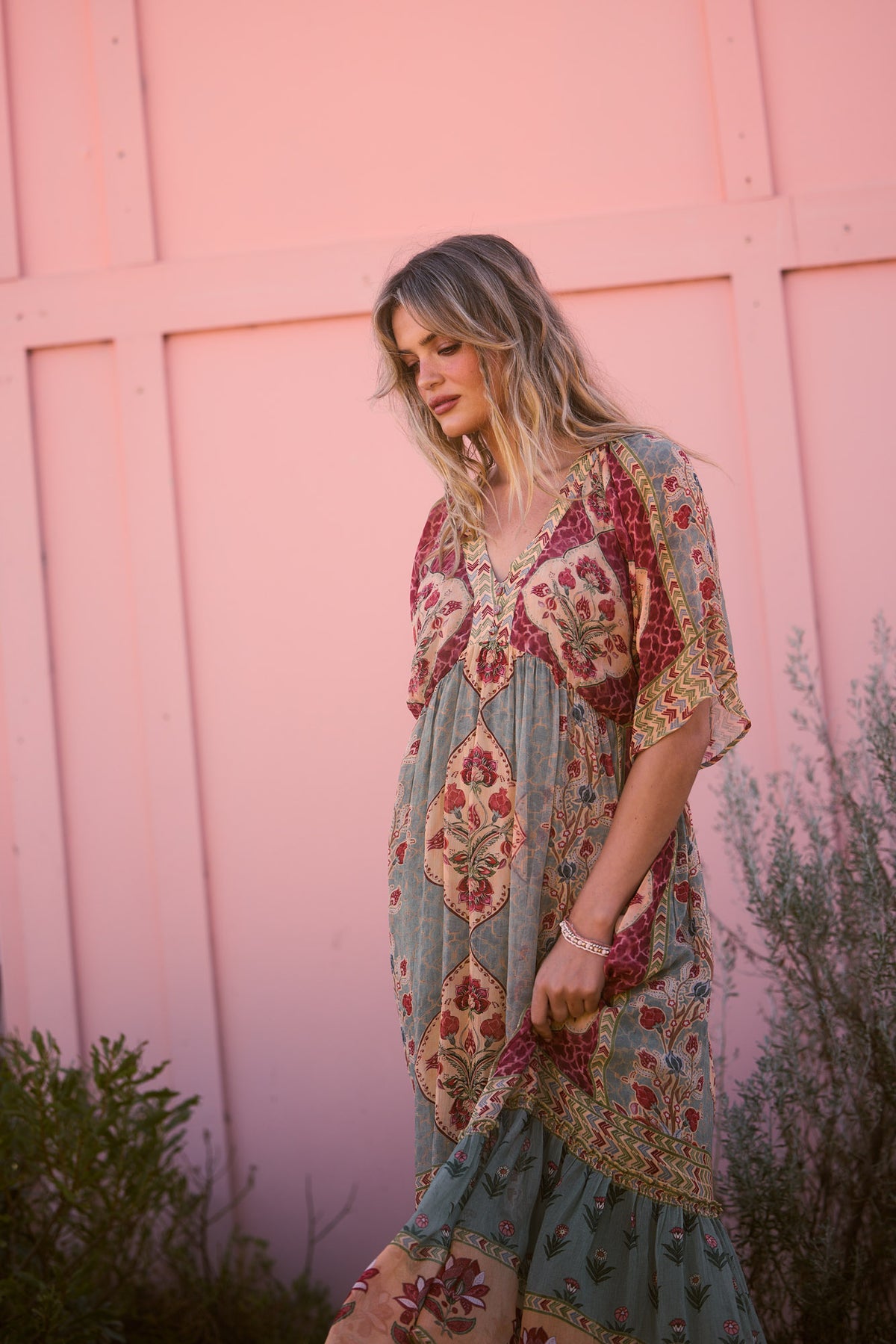 Tulara Dress in garden mist, against a pink wall with greenery.