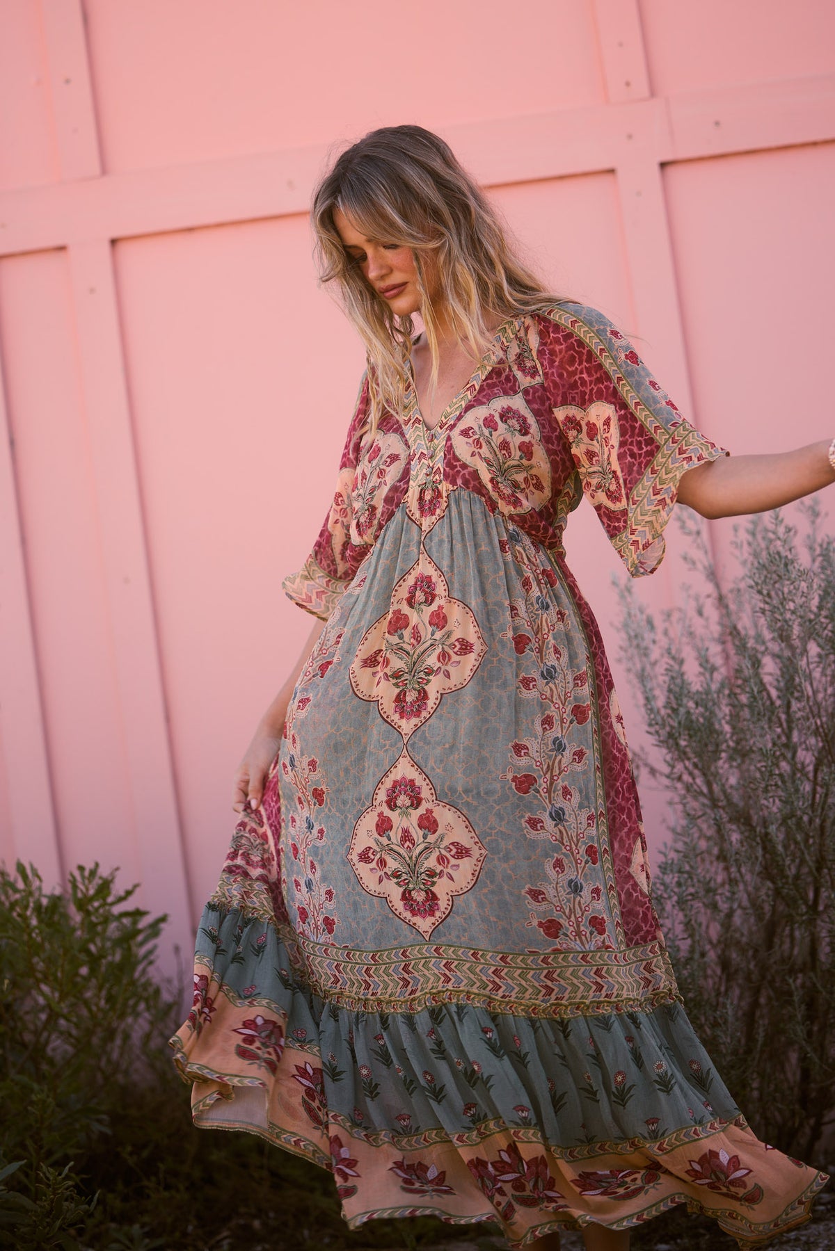 Tulara Dress in garden mist, twirling the skirt against a pink wall.