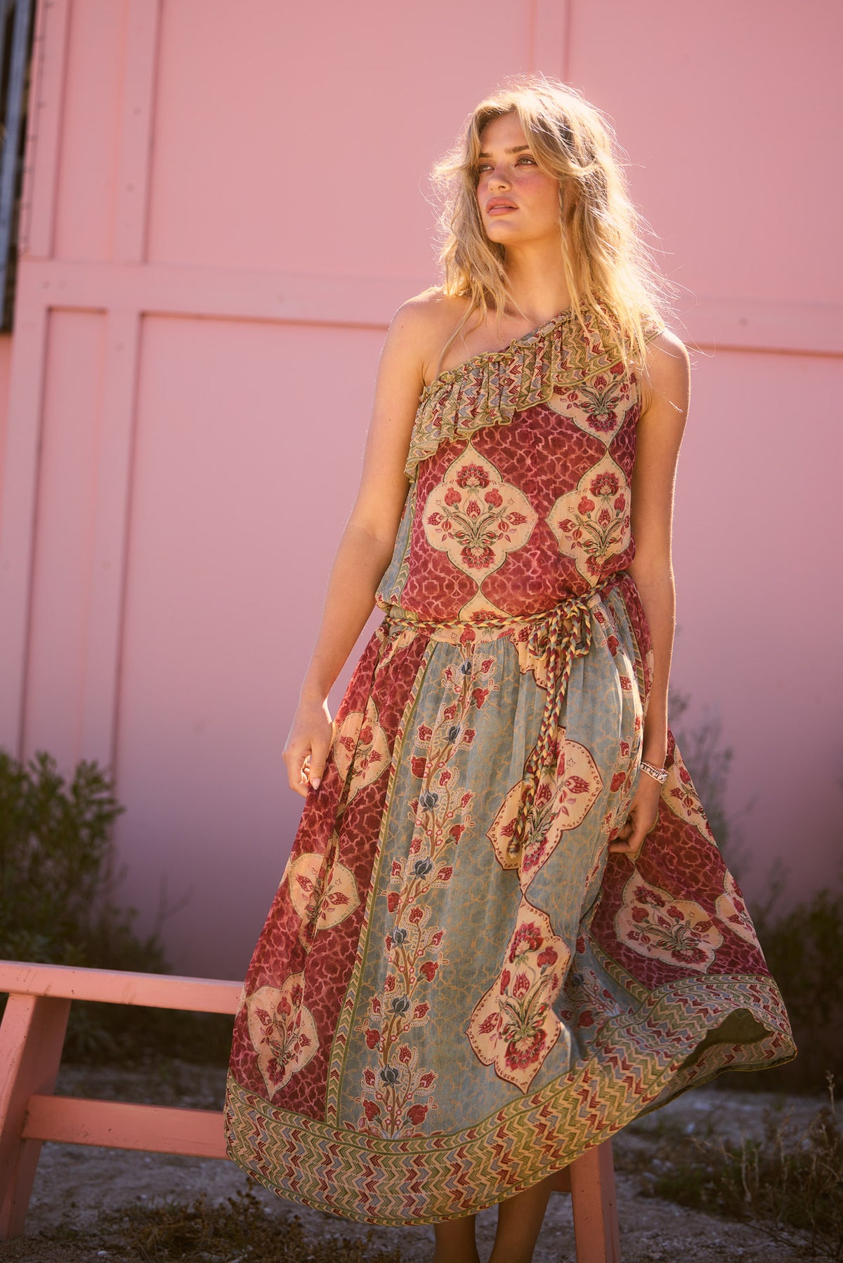Ravina Dress in garden mist, seated by a pink wall.