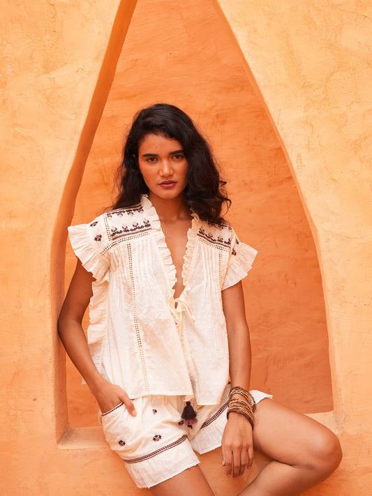 Saskia Tie Top and Saskia Short in natural dobby, seated against a terracotta wall.