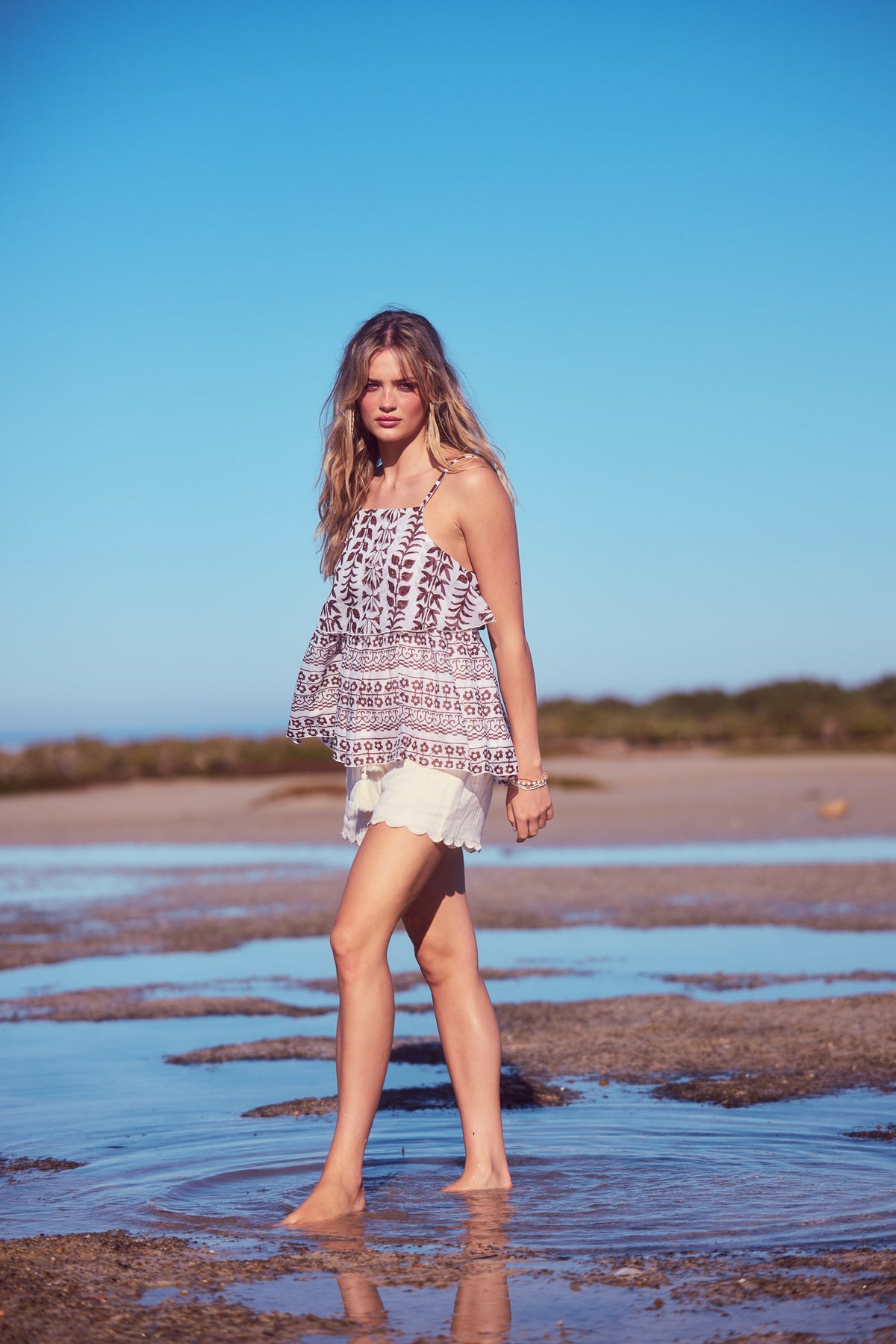 Rue Cami Top in chocolate paro, standing in shallow water under a blue sky.