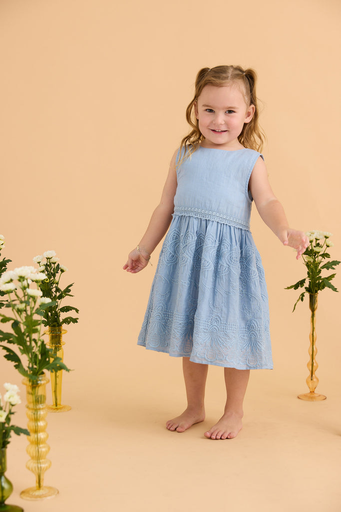 Young girl in a light blue dress standing between two flower vases on a beige background