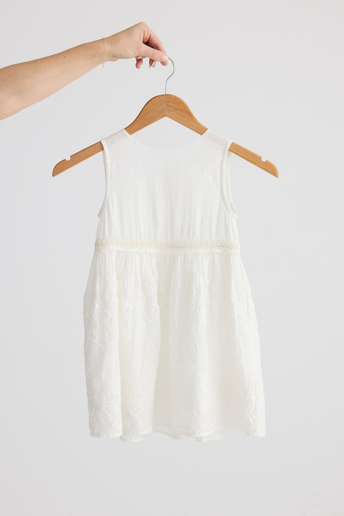White little girls dress on a hanger against a plain background