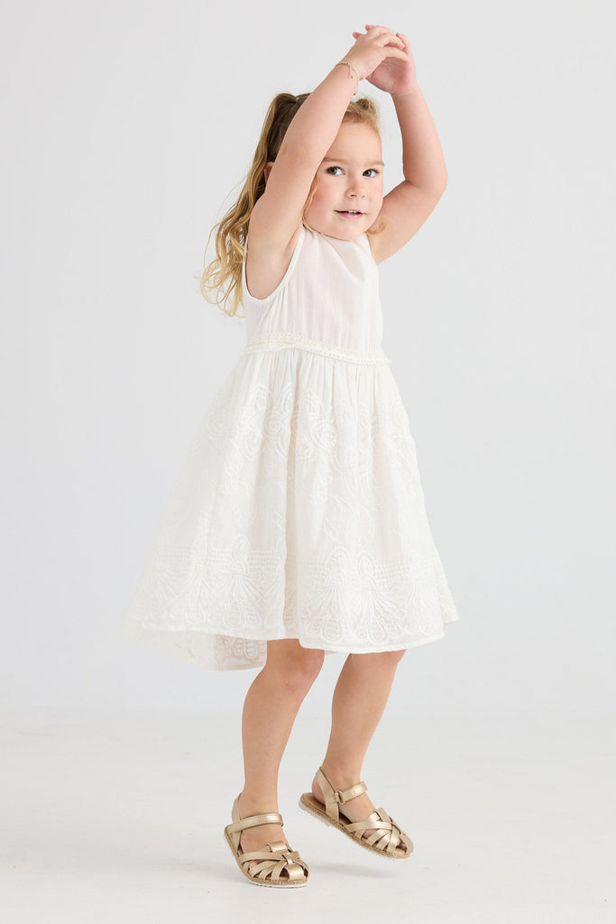 Young girl in a white dress standing against a plain background