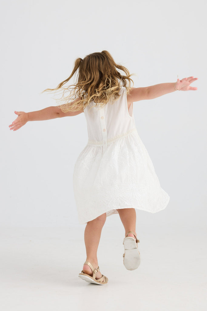 Young girl in a white dress standing with arms outstretched on a light gray background