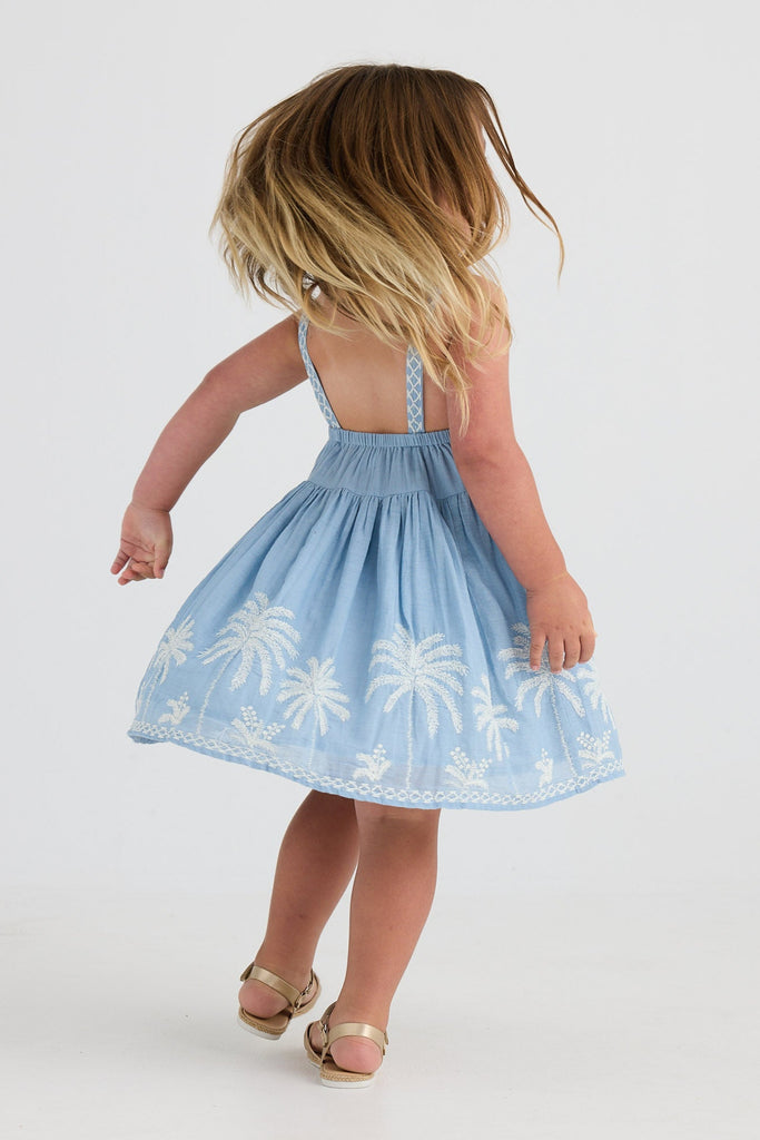 Child wearing a light blue dress with palm tree patterns on a white background