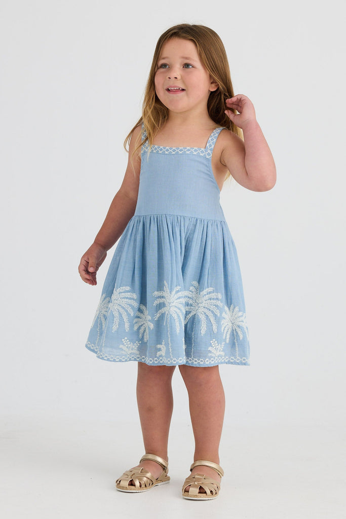 Young girl wearing a light blue dress with palm tree design on a white background