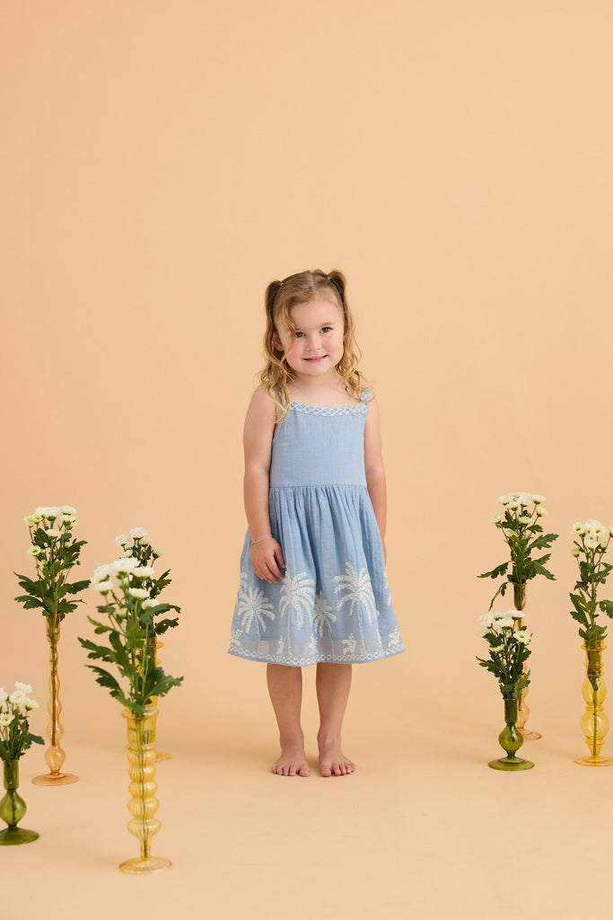 Young girl in a blue dress standing between floral arrangements on a beige background