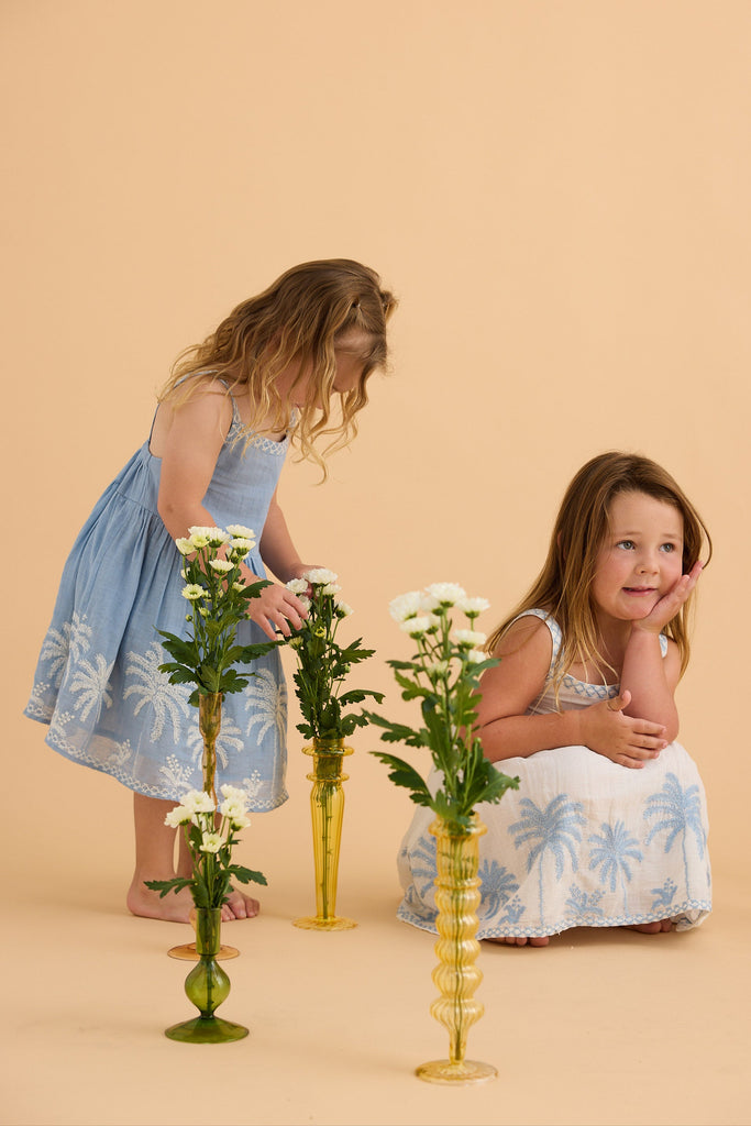 Two women in matching dresses with floral patterns standing next to vases on a beige background