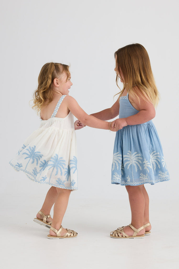 Two children in matching dresses holding hands against a white background